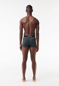 Grijze boxershorts met een zwarte tailleband waarop "LACOSTE" in het wit staat. Glad materiaal, strakke pasvorm en geen zichtbare patronen.