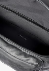 Black leather bag interior with smooth texture; features a logo "YOURTURN" printed in gray on the bottom, with a zipper compartment.