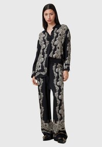 Sorte silk pyjamasett med intrikate sølv paisley-mønstre. Skjorten har knap-lukking foran, mens buksene har elastisk liv.