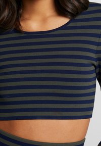 Striped crop top in navy blue and olive green, featuring a ribbed texture and a wide neckline, with a cropped length that exposes midriff.