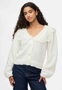 Vit cardigan med en scalloped spetskrage, stora knappar och ribbade manschetter. Mjuk textur med avslappnad passform och långa ärmar.