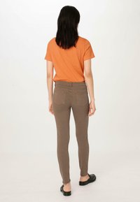 Oranje shirt met korte mouwen in combinatie met slim-fit bruine broeken. De broeken hebben achterzakken en een soepele textuur. Zwarte platte schoenen maken de look compleet.