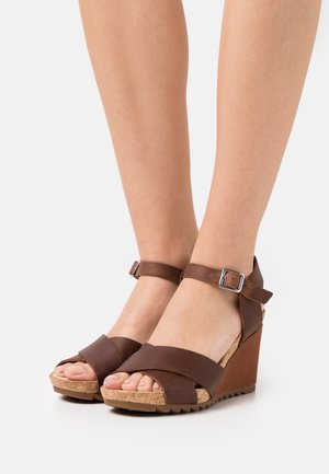 Bruine wedge sandalen met kurken zool, voorzien van brede kruisspanners en een verstelbare enkelriem met een metalen gesp. Getextureerd oppervlak.