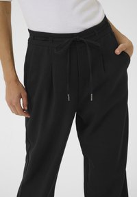 Pantalon noir en tissu lisse et léger avec une taille à cordon de serrage, des plis avant et des poches latérales. Accents matériels minimalistes.