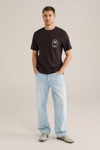 Zwarte katoenen t-shirt met een ronde halslijn, voorzien van een witte palmboomprint op de linkerkant van de borstzak. Lichtblauwe casual denim jeans.