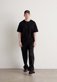 Camiseta negra de gran tamaño con manga corta, pantalones cargo negros y zapatillas deportivas negras. Una gorra negra con acentos de logo en blanco completa el conjunto.