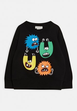 Schwarzer Pullover mit bunten Cartoon-Buchstaben U und kreisförmigen Figuren mit Armen, Augen und ausdrucksstarken Gesichtern in Blau, Grün, Gelb und Orange.