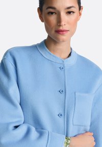 Svetlomodra flis jakna z ovratnikom, zapiranjem na gumbe in prsnim žepom. Mehka tekstura z udobnim prileganjem ter okroglimi gumbi.