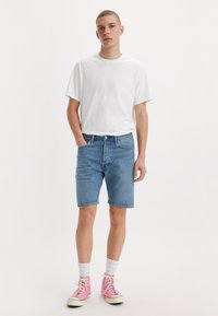 Men's casual outfit featuring a white T-shirt, blue denim shorts, and pink sneakers with white socks. Smooth cotton material and classic fit.