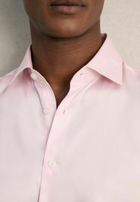 Chemise rose clair à col structuré, fermeture à un bouton et texture de tissu lisse. Présente des détails de coutures subtils.