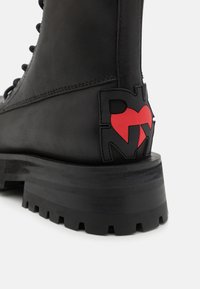 Svart lærkampstøvel med en kraftig gummisål. Har en rød og svart logo detalj på hælen og snøring foran.