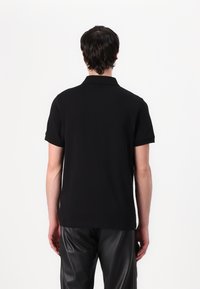 Zwarte polo-shirt met korte mouwen en een kraag, gemaakt van een gladde stof. Eenvoudig ontwerp, geen patronen of opvallende details zichtbaar op de achterkant.