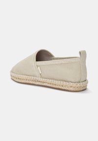 Beige canvas espadrille med rund tå og elastisk åbning i siden. Har en jute-indpakket sål og et lille stofmærke på siden.