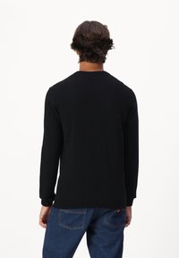 Schwarzer Strickpullover mit langen Ärmeln, Rundhalsausschnitt und gerippten Bündchen, kombiniert mit blauen Jeans, von hinten betrachtet.