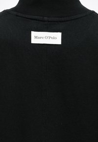 Μαύρο ζιβάγκο που φαίνεται από την πλάτη με λευκή ορθογώνια ετικέτα που γράφει “Marc O’Polo” κοντά στον γιακά.