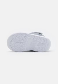 Bílá gumová podešev s texturovaným povrchem, zdobená složitými dezénovými vzory a výrazným logem značky vyraženým na boku.