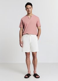 Maglietta henley a maniche corte rosa con tre bottoni, abbinata a pantaloncini bianchi comodi e sandali neri traforati. Tessuto liscio e vestibilità casual.