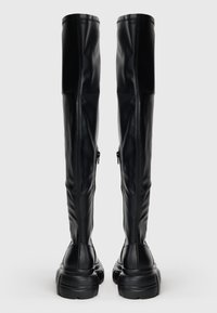 Μαύρες μπότες πάνω από το γόνατο, κατασκευασμένες από λεία τεχνητή δερμάτινη ύλη, με στρογγυλή μύτη, χοντρό πέλμα και φερμουάρ στις πλευρές.