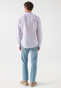 Lichtpaarse lange mouw shirt van textuurstof, met knoopmanchetten en een afgeronde zoom, gecombineerd met lichtblauwe rechte spijkerbroeken en beige schoenen.