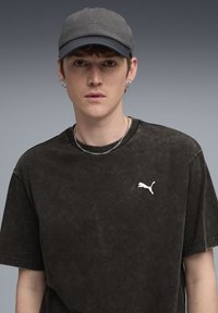 Sort, oversized T-shirt med en falmet tekstur, prydet med et hvidt Puma-logo. Grå kasket med et tekstureret design og buet skygge. Sølv kædetrøje.
