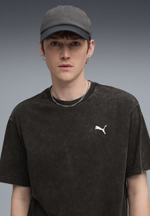 Black, oversized T-shirt with a faded texture, featuring a white Puma logo. Gray cap with a textured design and curved brim. Silver chain necklace.