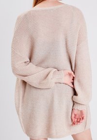 Ljusbeige oversized stickad tröja med ribbat mönster, uppvikta ärmar och sidsprund, som har en lös passform och mjukt tyg.