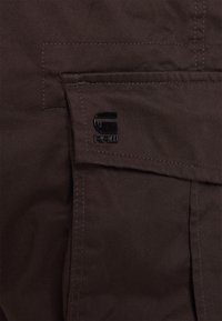 Bruna tyg cargo-shorts med ficka på vänster sida som har en svart G-Star RAW-logotyp, synliga sömmar och en strukturerad design.