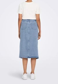 Světle modrá dlouhá džínová sukně s rovný střihem, která má zadní kapsy a roztrhaný lem. Kombinována s bílým přiléhavým tričkem a bílými teniskami.