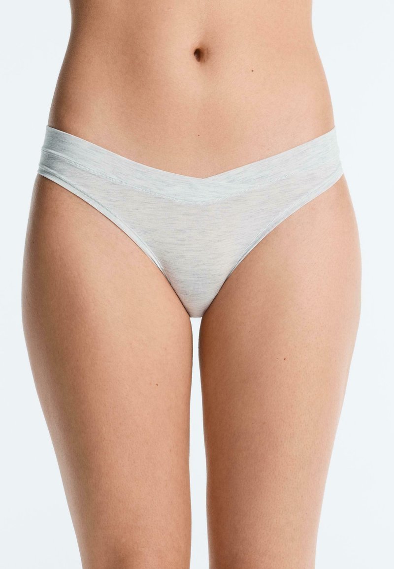 Torso féminin portant un sous-vêtement bikini en coton gris clair sur un fond blanc uni.