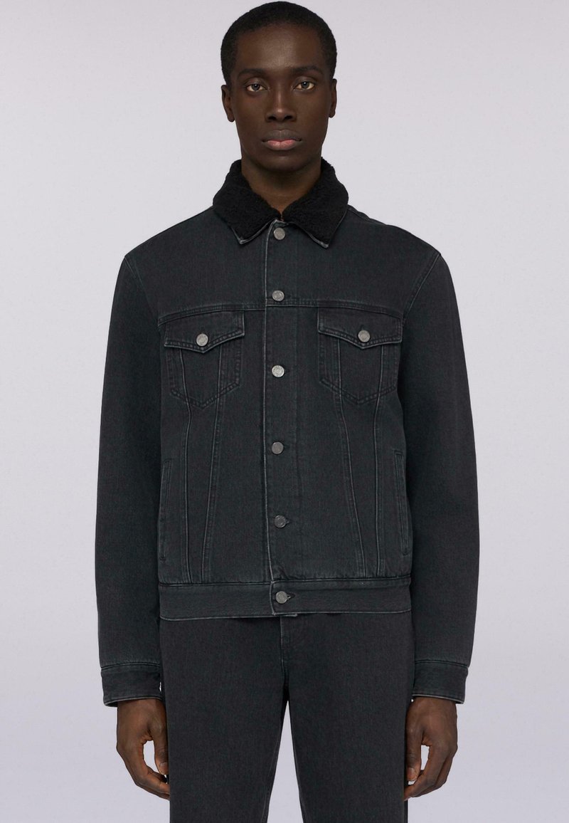 Giacca in denim nera con colletto testurizzato nero, chiusura frontale con bottoni e due tasche sul petto. Presenta un design aderente e un taglio dritto.