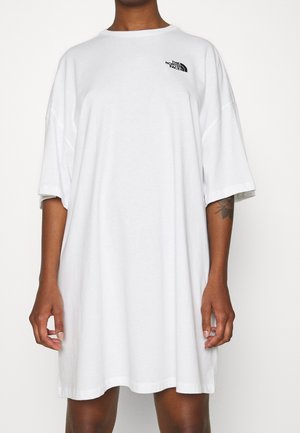 Osoba nosząca za dużą, białą sukienkę typu t-shirt marki The North Face z krótkimi rękawami i małym czarnym logo na piersi.