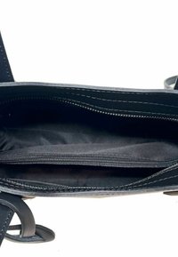 Vnitřek černé kožené kabelky obsahující zipovou kapsu, hladkou texturu, jemné detaily šití a dvě otevřené přihrádky.