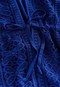 Haină din dantelă albastră cu modele florale detaliate, o panglică din satin în talie și o textură moale a țesăturii.