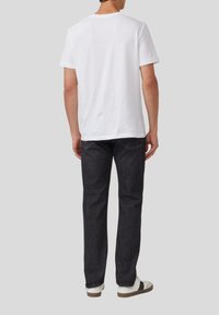 Weißes Baumwoll-T-Shirt mit kurzen Ärmeln, kombiniert mit dunklen Jeans. Die Jeans haben ein schlichtes Design und sind mit weißen Sneakers gestylt.