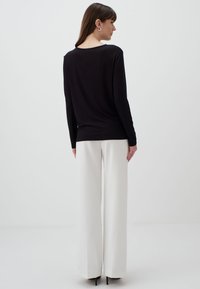 Zwarte lange mouwen top met een ontspannen fit en een ronde halslijn, gecombineerd met hoge taille, wijde witte broeken. Soepele textuur, minimalistisch ontwerp.
