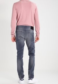 Vaqueros de mezclilla gris con un diseño ajustado, cinco bolsillos y una textura desgastada. Combinados con una blusa de manga larga rosa claro y zapatillas blancas.