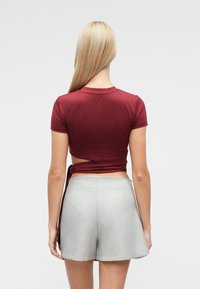 Soonikuga sügavpunane lühikeste varrukatega särk avatud seljaga, mis on kombineeritud helehallide kohandatud lühikeste pükstega. Pehme tekstuur, keha järgiv lõige ja puhtad jooned.