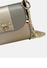 Beige en grijze leren handtas met een gouden bij-embleem, een kettinghengsel en een klein Italiaans vlaggetje charm dat aan de ritshendel hangt.