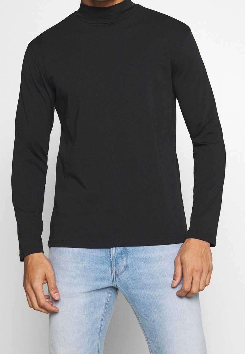 Schwarzes Langarm-Turtleneck-Shirt aus glattem Stoff, mit figurnahem Schnitt und schlichter Verarbeitung. Kombiniert mit hellblauen Jeans.