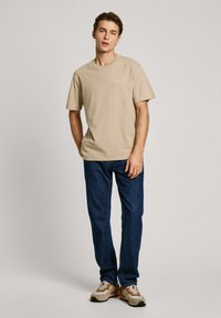 Beige cotton t-shirt with short sleeves and a round neck, paired with dark blue denim jeans and beige sport shoes with brown accents.