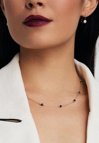 Srebrny łańcuszek naszyjnik z maleńkimi czarnymi koralikami, prezentujący delikatny wzór. Para minimalistycznych srebrnych kolczyków z przezroczystymi kamieniami.