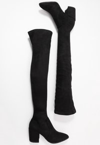 Bottes noires au-dessus du genou avec un bout pointu, un talon bloc et une texture en daim lisse. Les bottes sont ajustées et sans couture le long de la jambe.