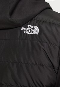 Sort pufferjakke med hætte, med en sømløs panelopdeling. Hvid broderet logo på venstre skulderområde. Glat, mat tekstur.