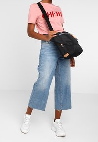 Borsa a tracolla nera con design a patta, dettagli color cammello, tessuto testurizzato, tracolla regolabile e tasca frontale con zip.