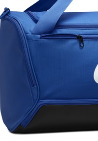 Blauwe sporttas gemaakt van gestructureerde stof met een zwarte onderkant. Heeft dubbele bovenritsen en een groot logo-accent. Verstelbare schouderriem.