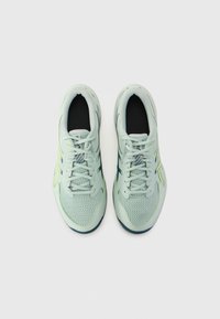 Baskets de sport vert clair avec une tige en maille, des accents vert foncé contrastants et une semelle texturée. Comprend un laçage standard et un col rembourré.