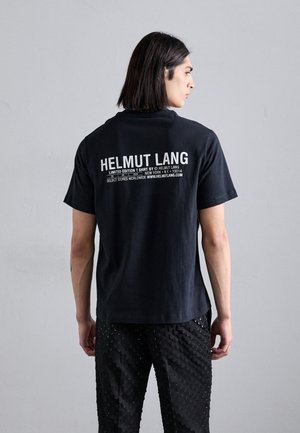Must musta T-särk musta puuvillast, millel on brändinimi "HELMUT LANG" ja valge tekst seljal. Mudel kannab tekstuuriga musti pükse.
