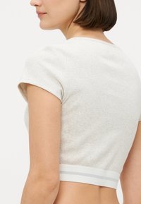 Ljust grått kort t-shirt i ribbad tyg, med korta ärmar och ett stretchy vitt band i fållen med gråa ränder.