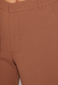 Rjave skrčene hlače z gladko teksturo, slim fit krojem in stranskimi žepi. Pas z zankami za pas za dodatno prilagodljivost.
