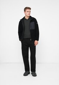 Black fleece jacket with zippered front and chest pocket, paired with dark grey polo shirt and black cargo pants featuring side zippers.